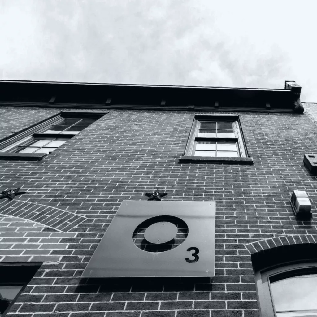 Greyscale, exterior shot of O3 office with logo on brick.