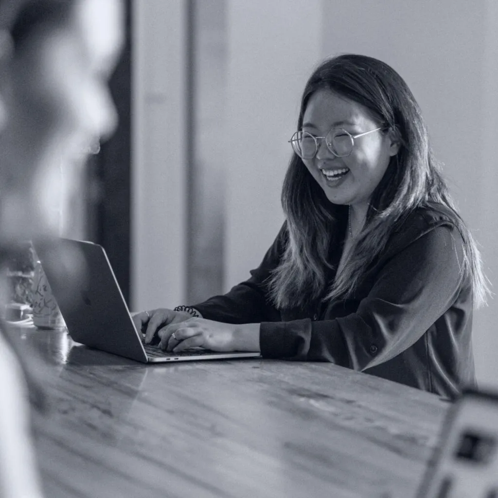 Two O3 employees in the office working face to face and smiling.