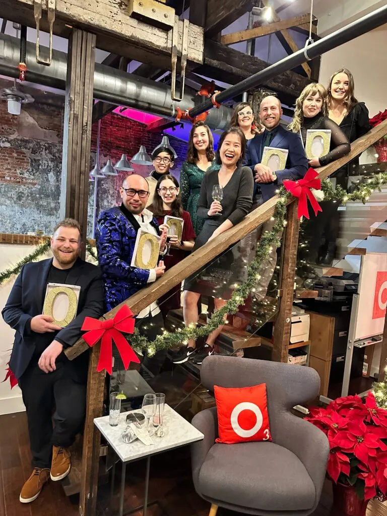 O3 employees standing on office staircase with golden glitter Os in hand.