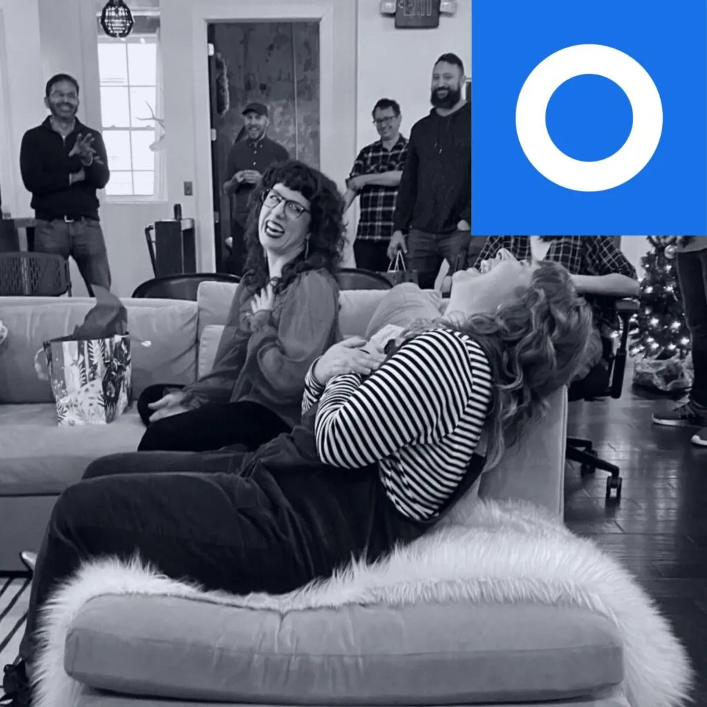 Two O3 team members sitting on a couch and laughing during gift exchange.